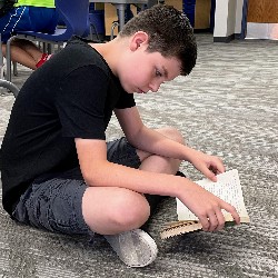 An HPES student sits on the library floor, reading a book.